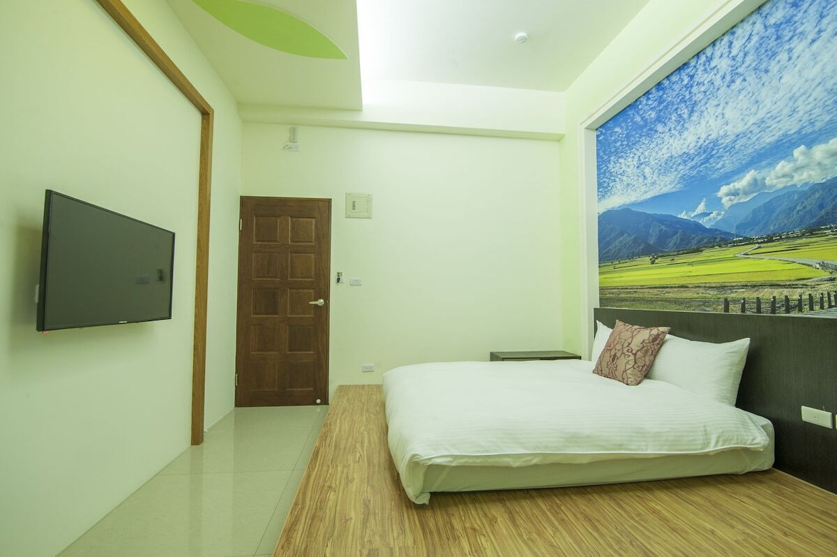 Un dormitorio con una cama, un televisor montado en la pared y una puerta.