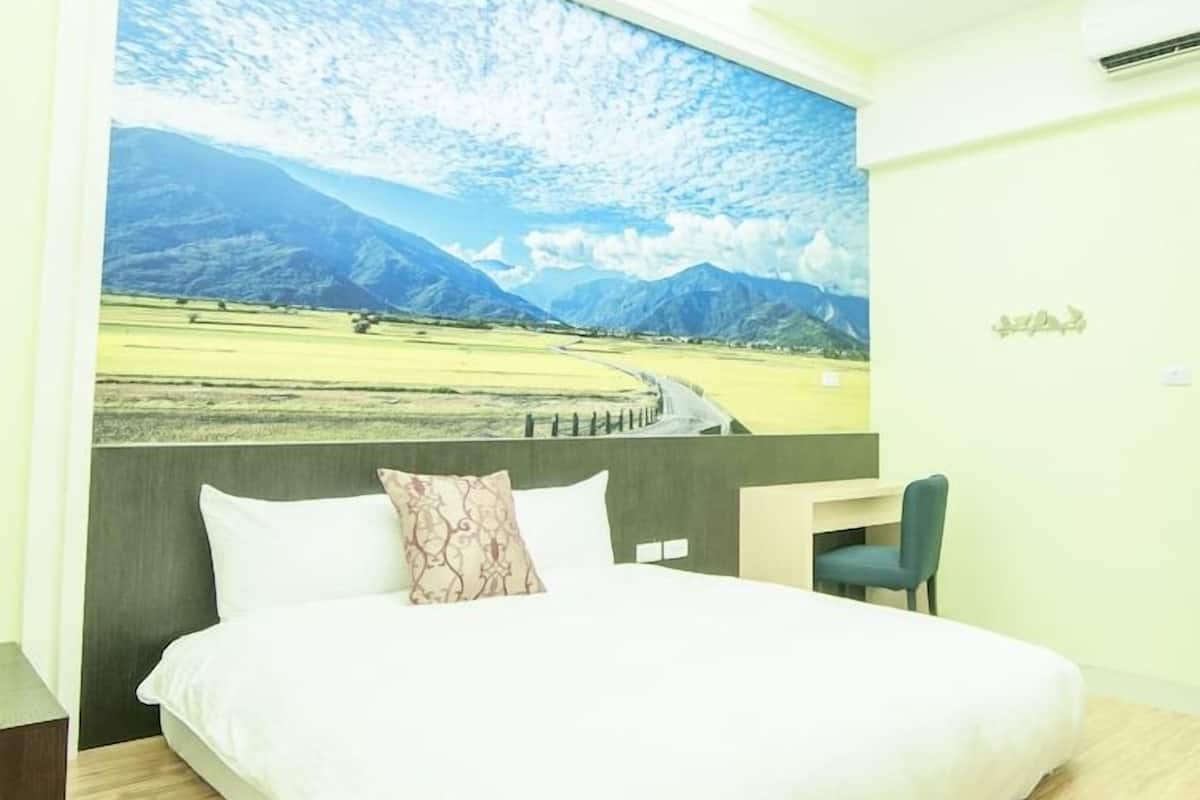 A bedroom with a large bed, a desk, and a chair. There is a window with a view of a landscape.