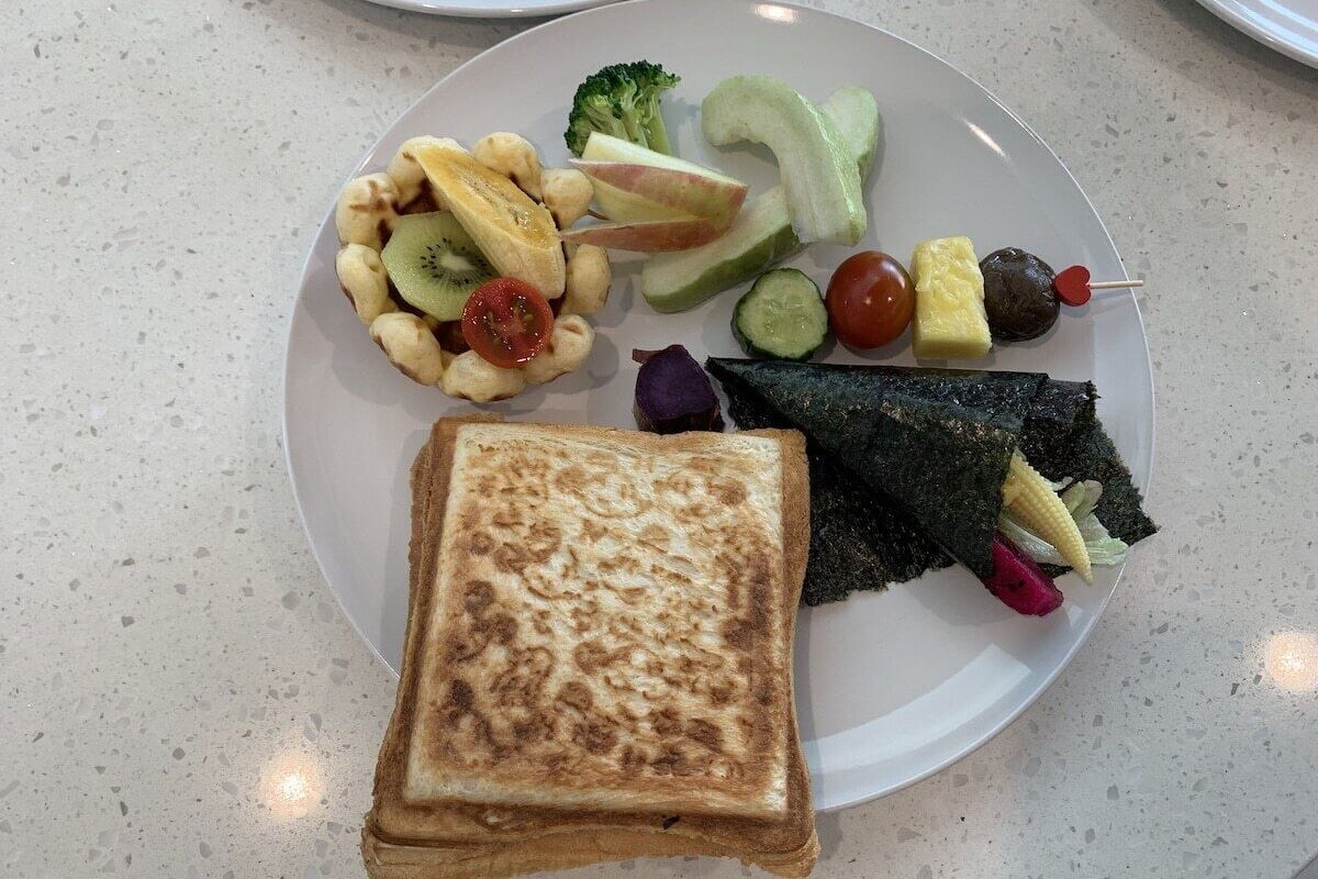 A plate with a grilled cheese sandwich, assorted vegetables, and a piece of fish.