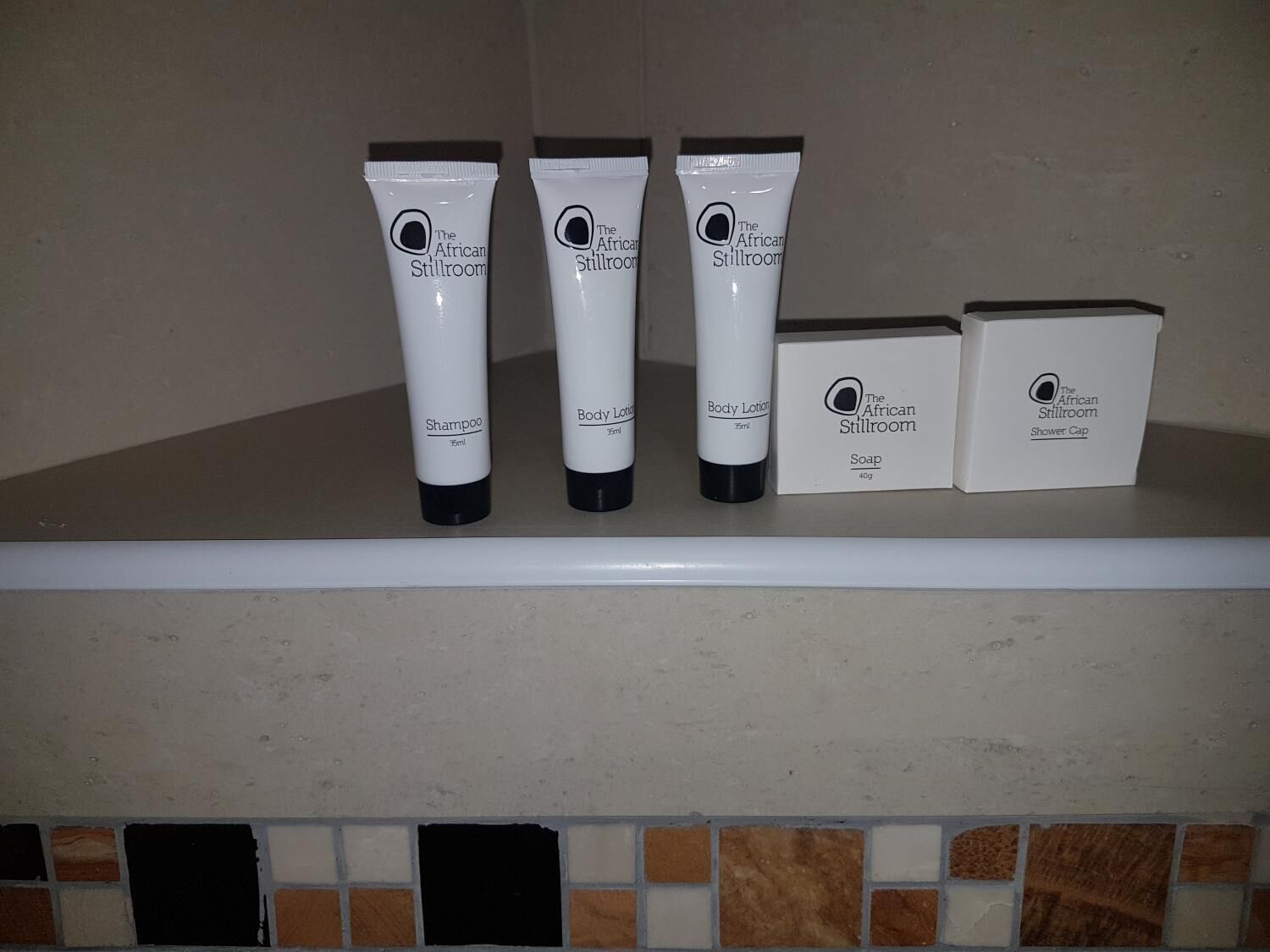 En hyldest i badeværelset med fire flasker The African Stillroom kropsplejeprodukter og en æske med hårbånd.