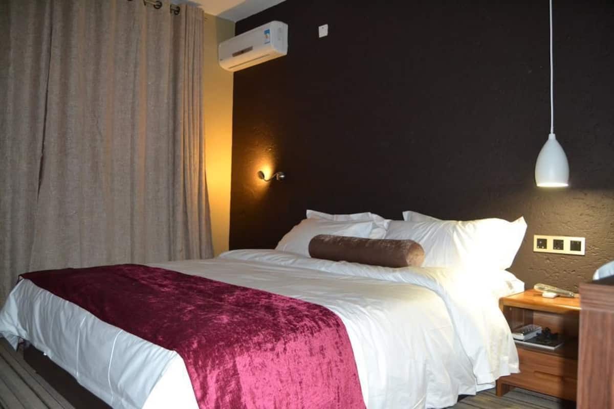 Quarto de hotel com cama, mesa de cabeceira, abajur e ar condicionado.