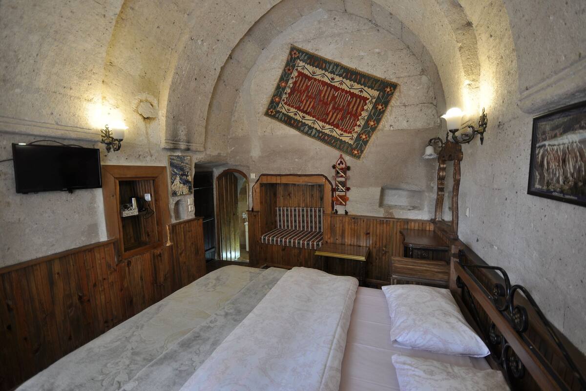 Ein Zimmer mit einem großen Bett, Holzmöbeln, einem Fernseher und einer einzigartigen, gewölbten Decke.