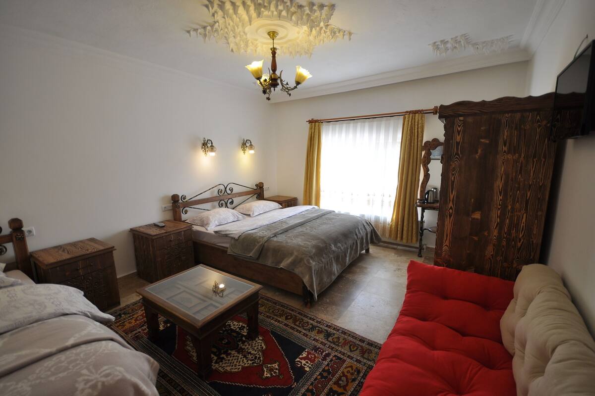 Ein Schlafzimmer mit einem hölzernen Bett, Nachttischen, einem Beistelltisch, einem roten Sofa, einem gemusterten Teppich und einer Pendelleuchte.