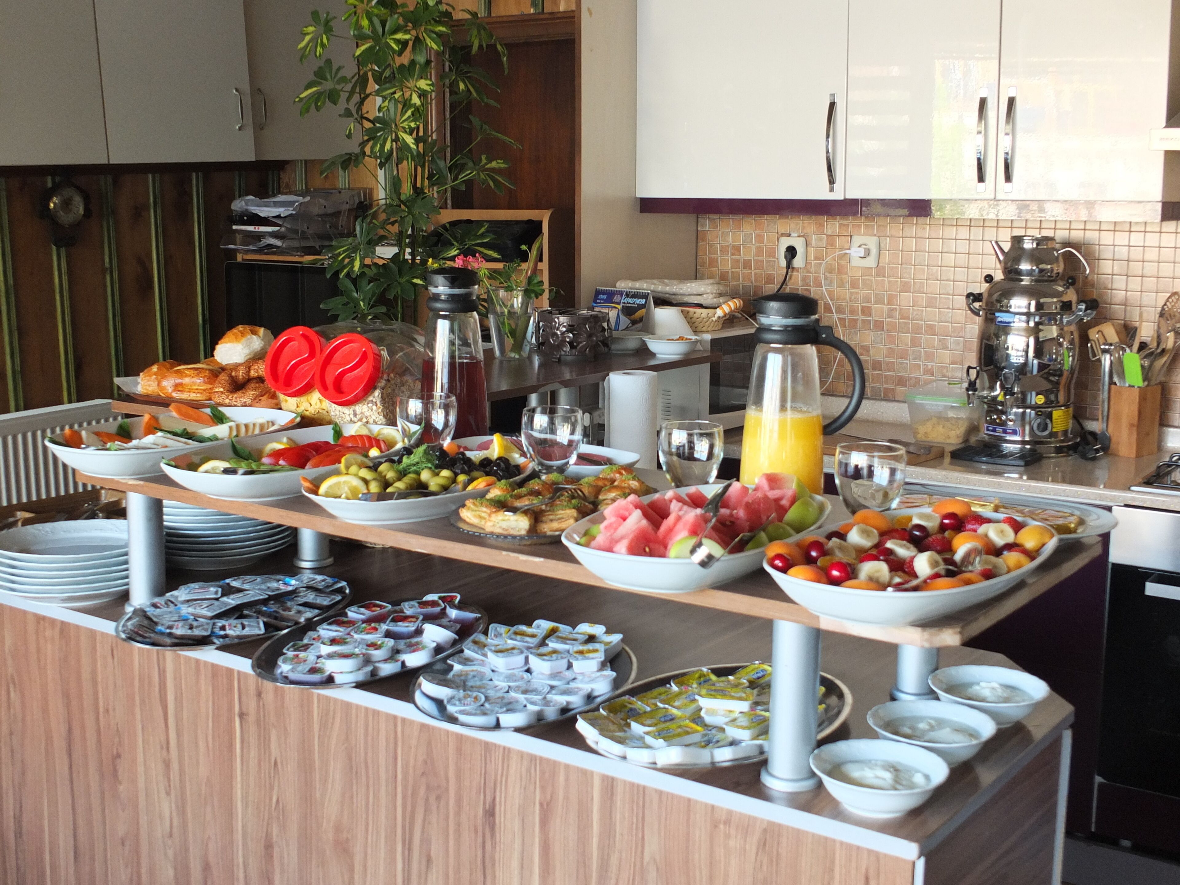 A buffet with various food items and beverages, a coffee maker, and a plant in the background.
