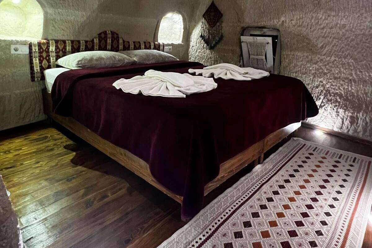 Ein Zimmer mit einem Bett, Holzboden, einem gemusterten Teppich und einem kleinen Fenster.
