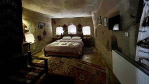 A cozy, rustic room with a large bed, a wooden nightstand, a small table, and a patterned rug.
