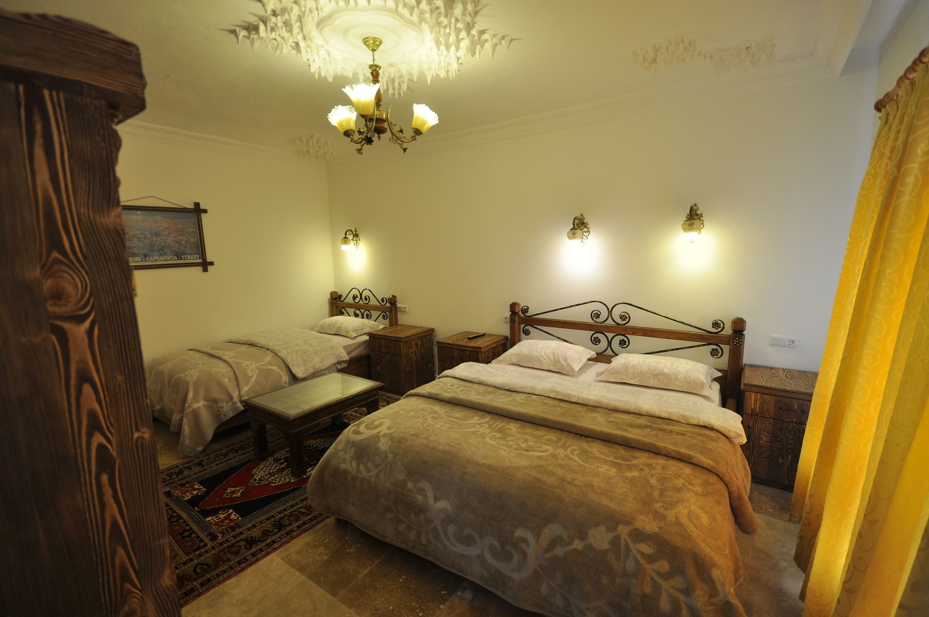 A bedroom with two beds, a chandelier, wall sconces, and a wooden headboard.