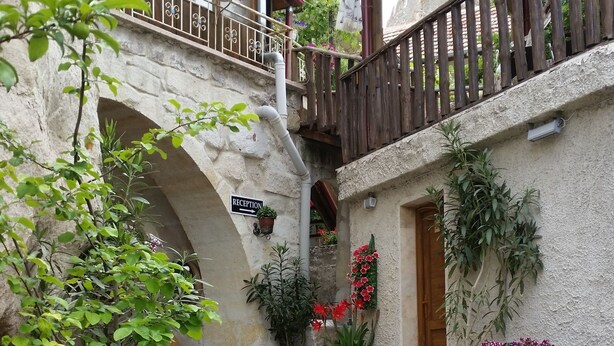 A stone courtyard with a wooden balcony, potted plants, and a rustic wooden bench.