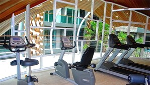 Uma academia com diversos equipamentos de exercício, janelas amplas e vista para o exterior.