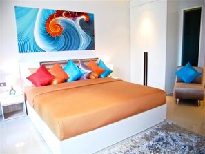 Une chambre à coucher moderne avec un grand lit, des coussins colorés, un élément décoratif mural, une chaise et un tapis.