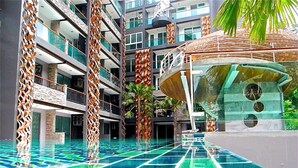 Área de piscina de hotel moderna com vários níveis, um elemento central de água e design tropical.