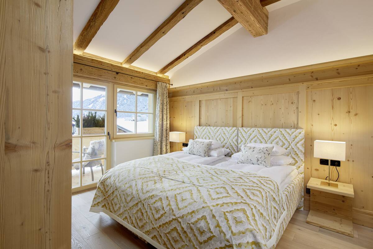 A bedroom with a large bed, wooden walls, a window with curtains, and a nightstand with a lamp.