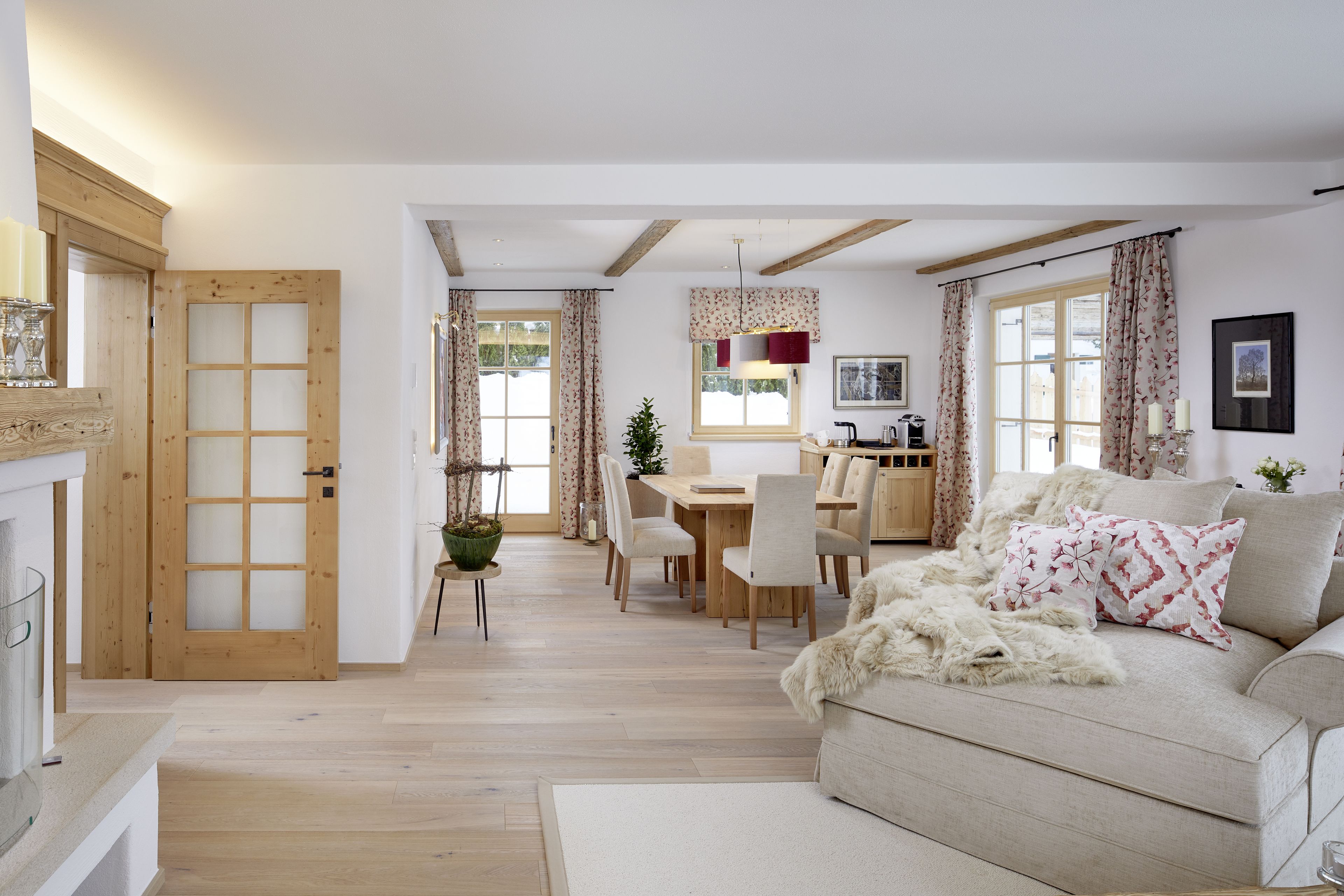 Amplia sala de estar con sofá, mesa de comedor y sillas. Se observa una puerta de madera y una ventana con cortinas.