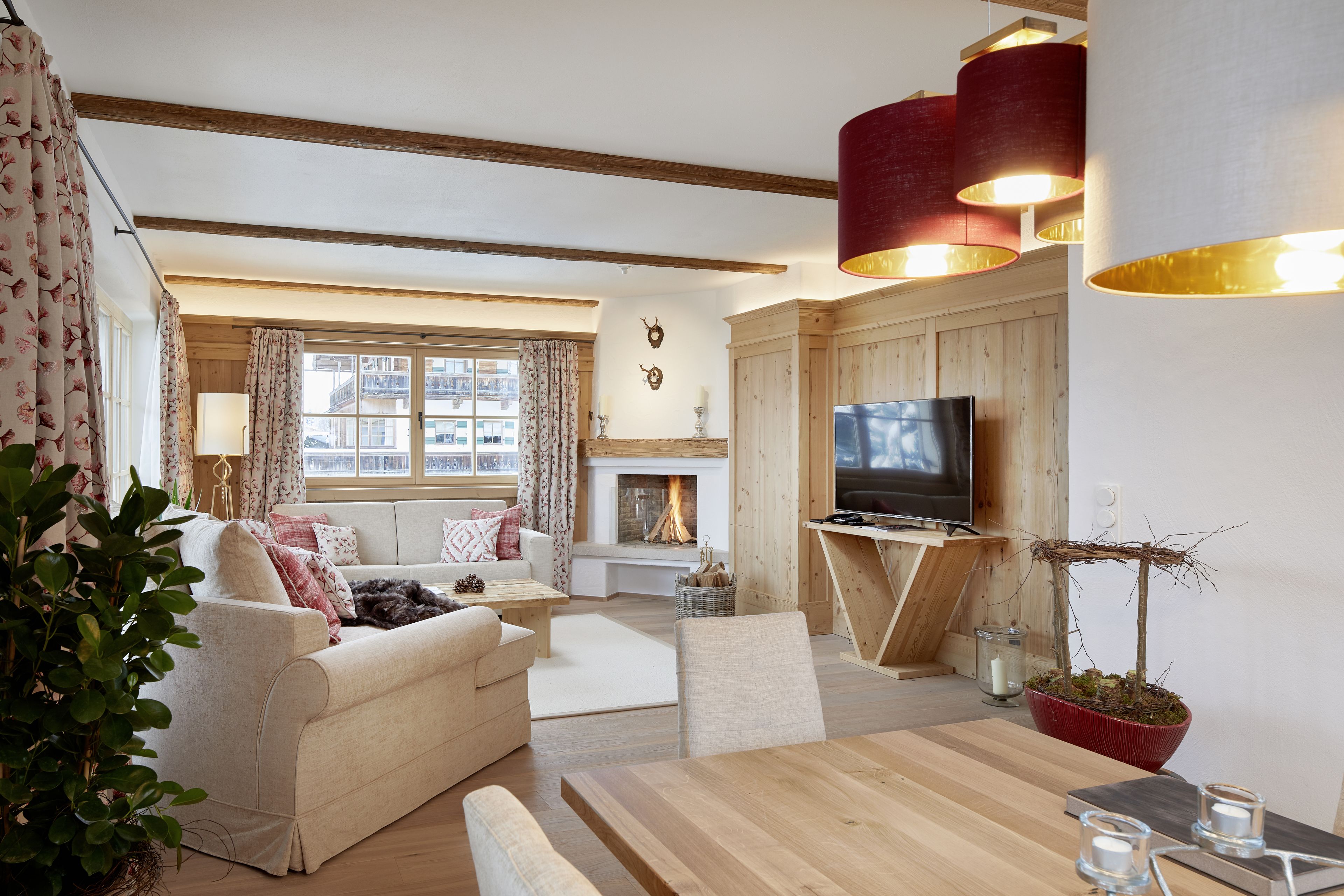 A cozy living room with a fireplace, wooden beams, a television, and a dining area.