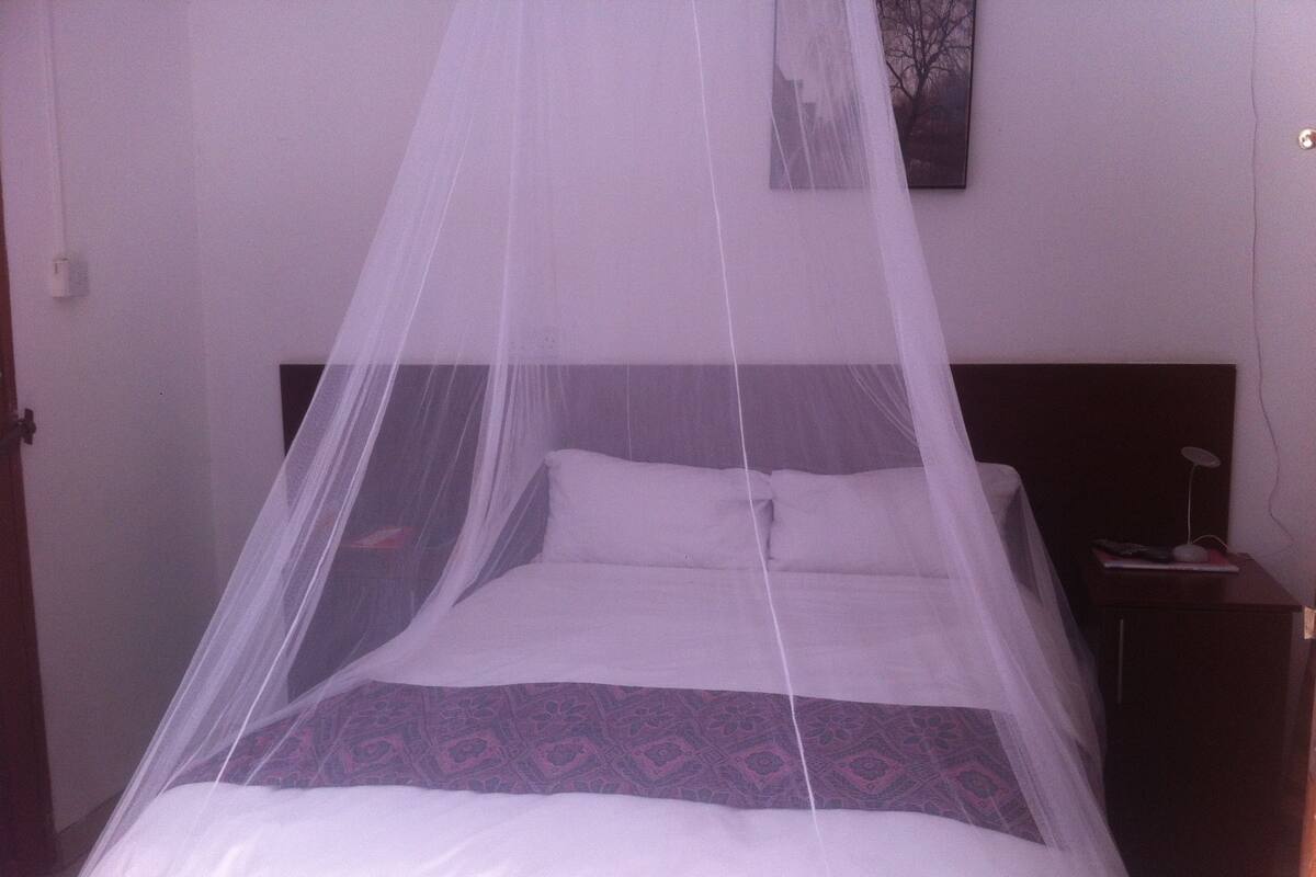 A bed with a canopy, a nightstand with a lamp, and a painting on the wall.