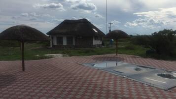 A thatched-roof building with a paved patio area featuring a metal table and chairs.
