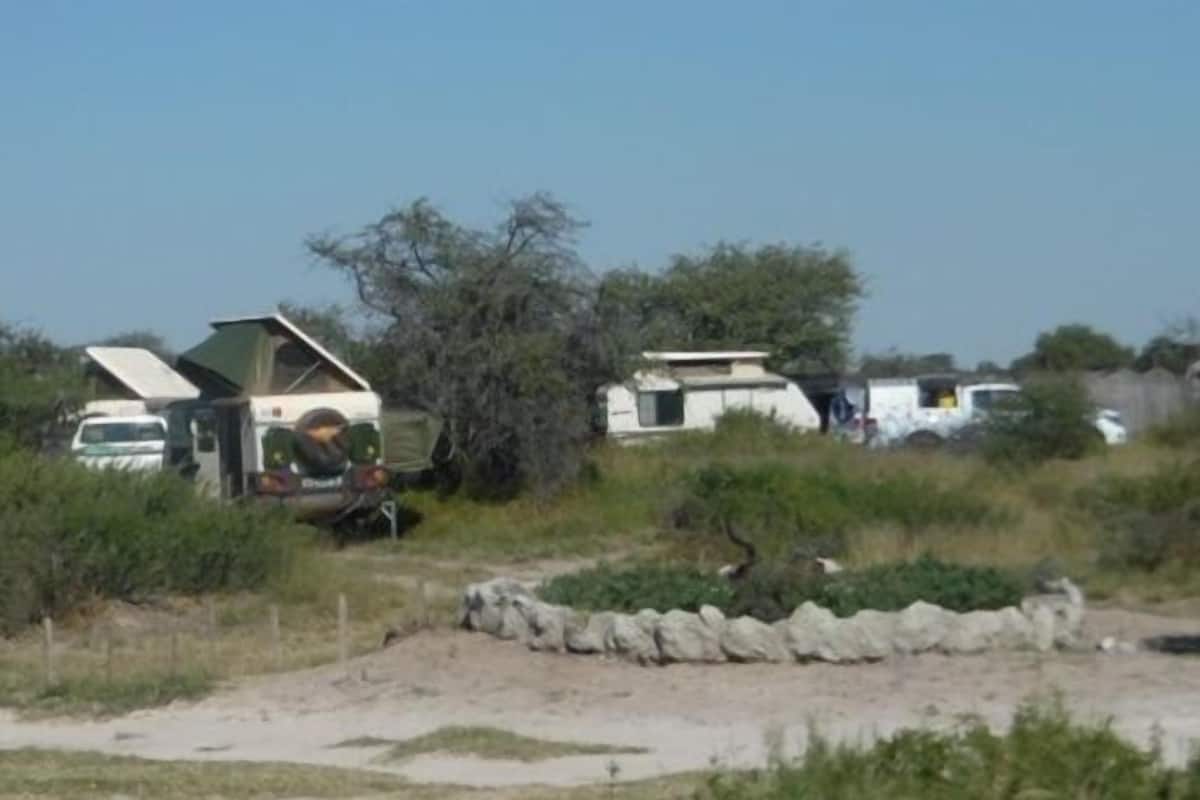 A campsite with RVs and tents, surrounded by sparse vegetation and a clear sky.