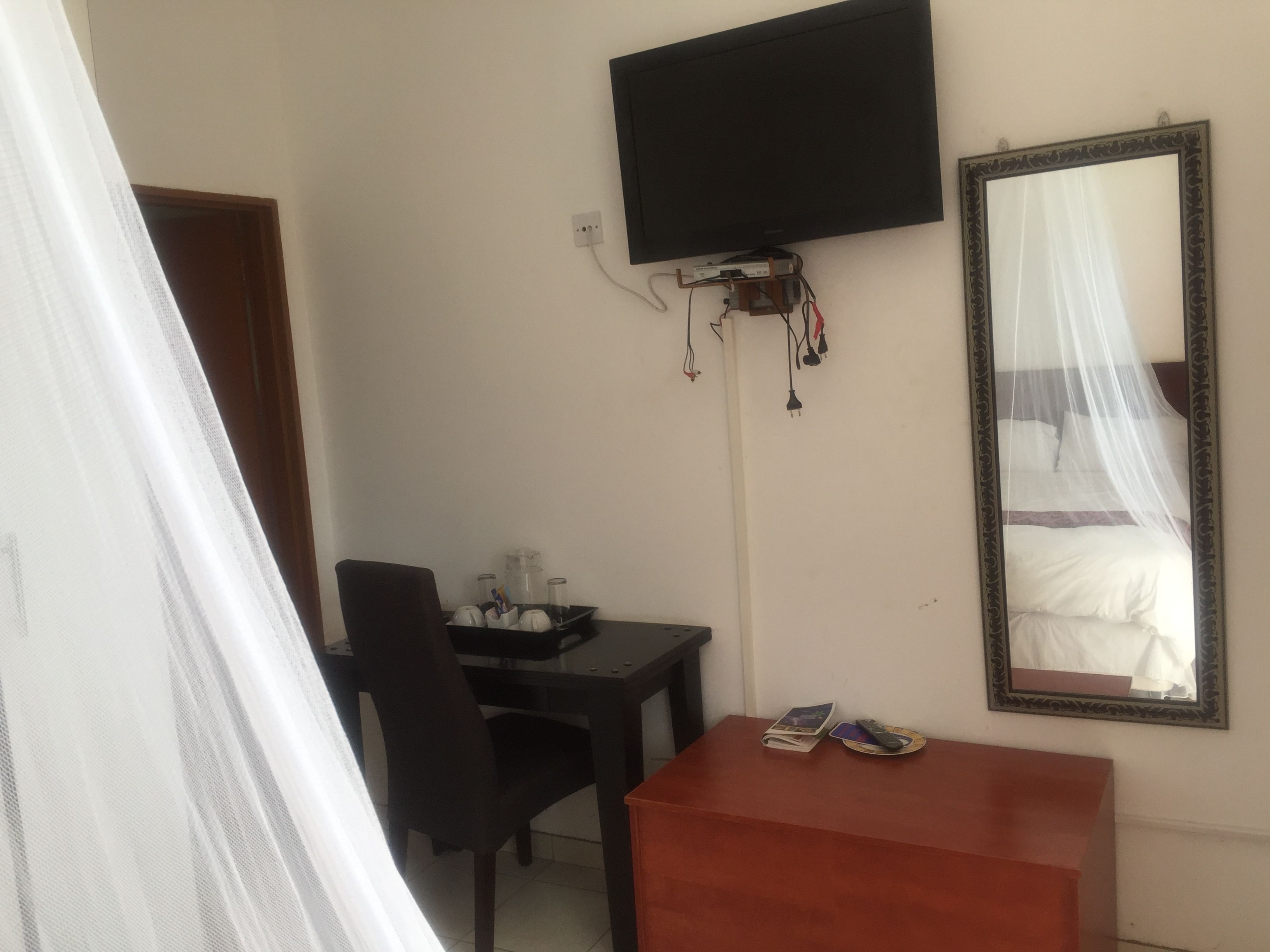 A hotel room with a bed, a desk, a chair, a TV mounted on the wall, and a mirror.