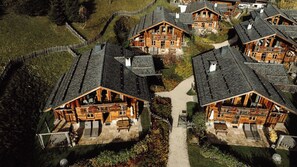 A cluster of wooden cabins with sloped roofs, a central pathway, and surrounding greenery. - Chaletdorf Auszeit (Huettschlag)