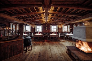 A rustic wooden interior with exposed beams, a fireplace, and a dining area with tables and chairs. - Chaletdorf Auszeit (Huettschlag)