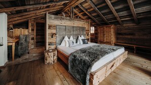 A rustic wooden cabin interior with a large bed, wooden walls, and a high ceiling. - Chaletdorf Auszeit (Huettschlag)