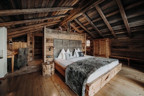 A rustic wooden cabin interior with a large bed, wooden walls, and a high ceiling. - Chaletdorf Auszeit (Huettschlag)
