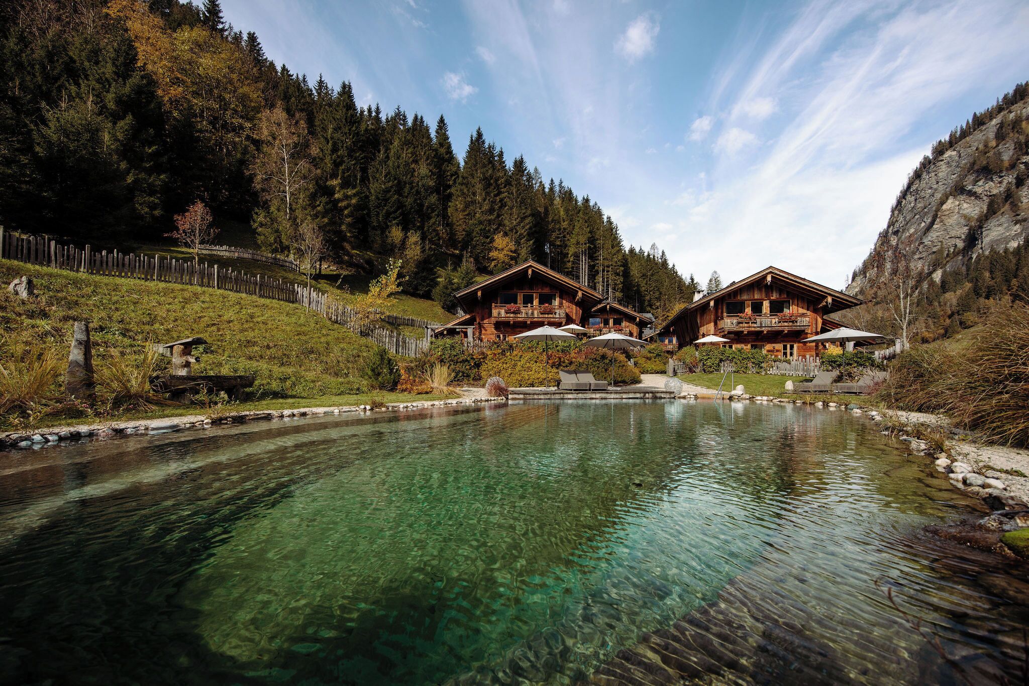 A mountain lodge with a clear pool, wooden cabins, and a forested backdrop.