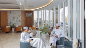 A modern hotel lobby with marble flooring, comfortable seating, large windows, and a city view. - Muscat Hills Hotel (Muscat)