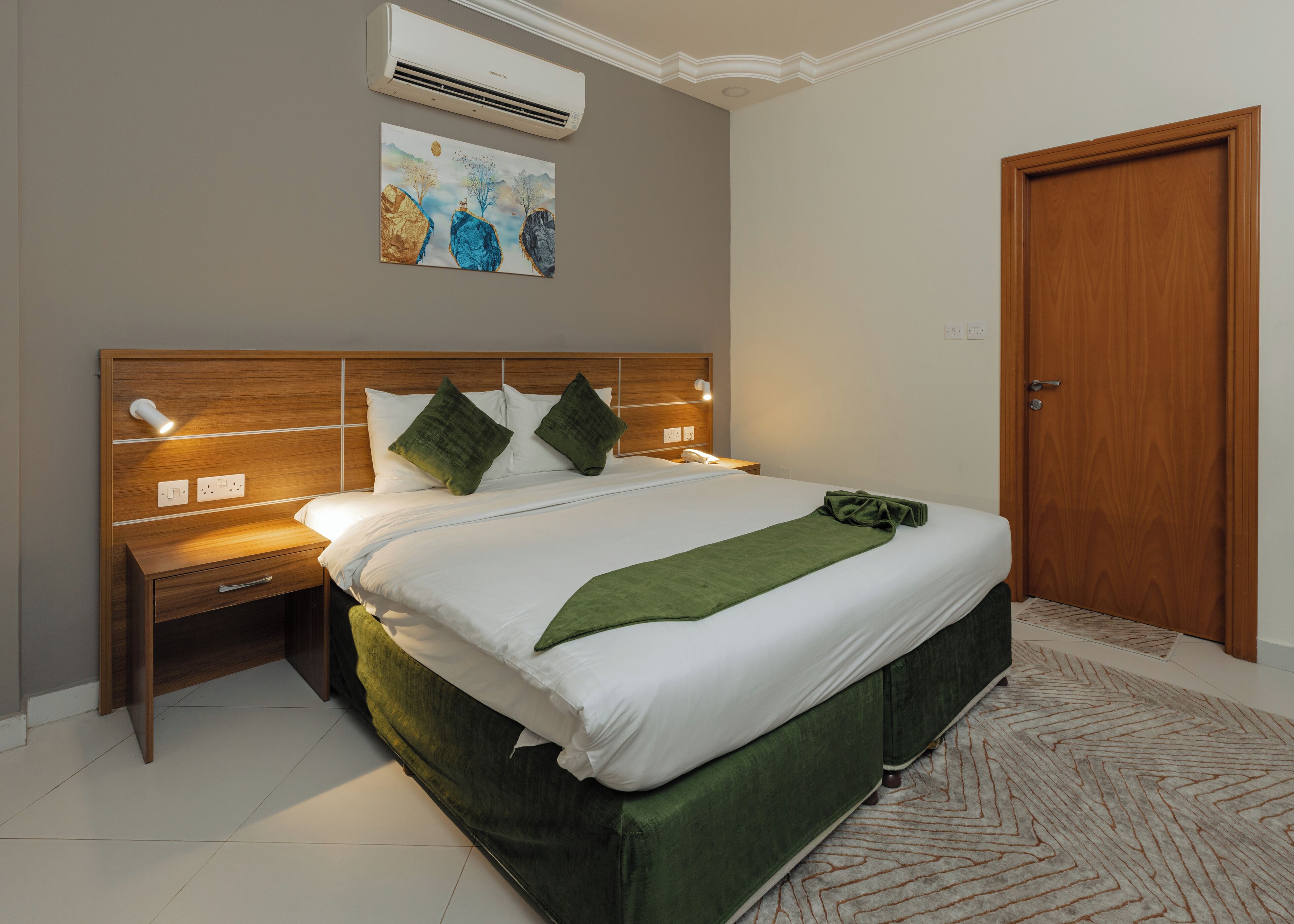 Una cama bien hecha con un plaid verde, un cabecero de madera y una mesita de noche con una lámpara.