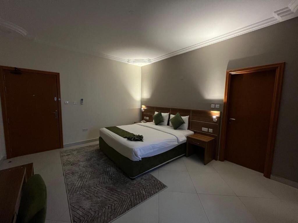 Un dormitorio con cama, mesitas de noche, alfombra y una puerta.