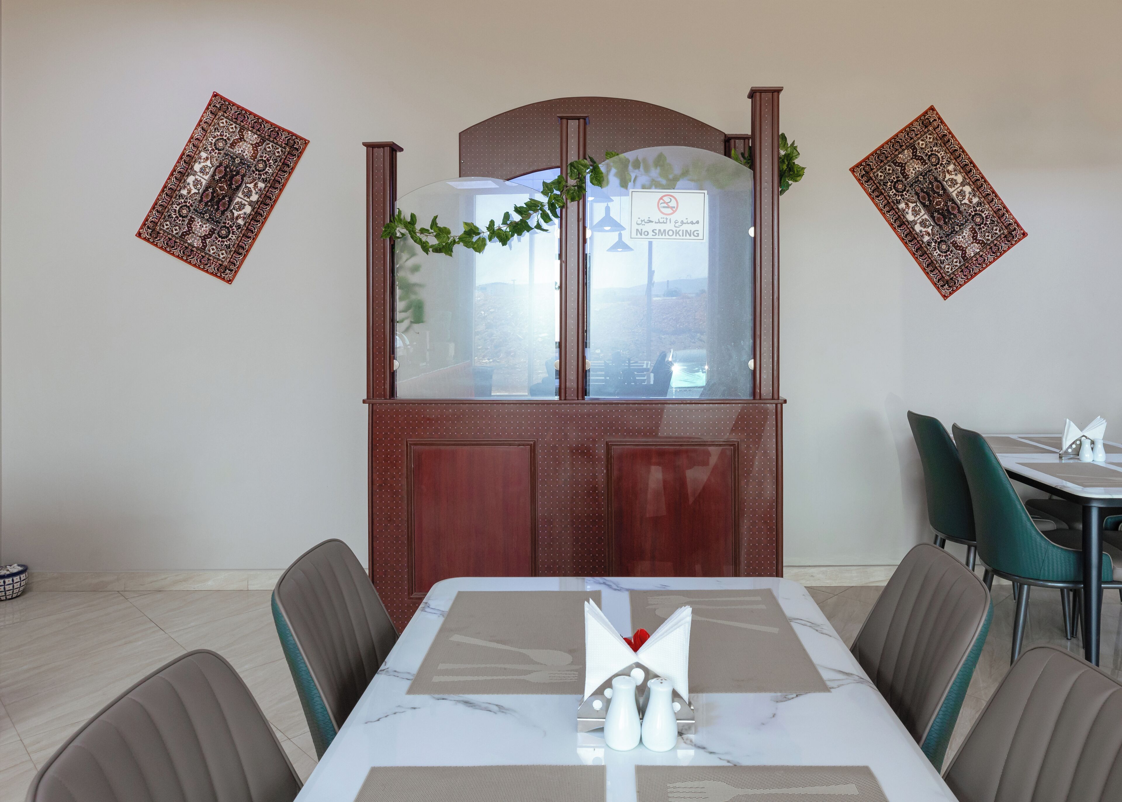 Een eethoek met een tafel gedekt voor twee personen, een houten kast met een matglazen deur, en twee decoratieve wandpanelen.