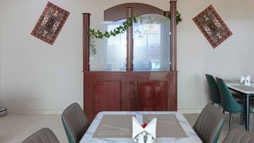 Een eethoek met een tafel gedekt voor twee personen, een houten kast met een matglazen deur, en twee decoratieve wandpanelen.