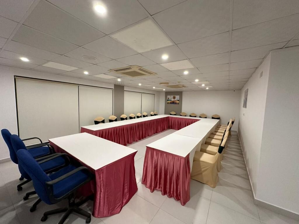Un salón de conferencias con una larga mesa, sillas azules y una pizarra.