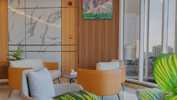 A modern lobby with marble walls, wooden paneling, and comfortable seating. - Muscat Hills Hotel (Muscat)