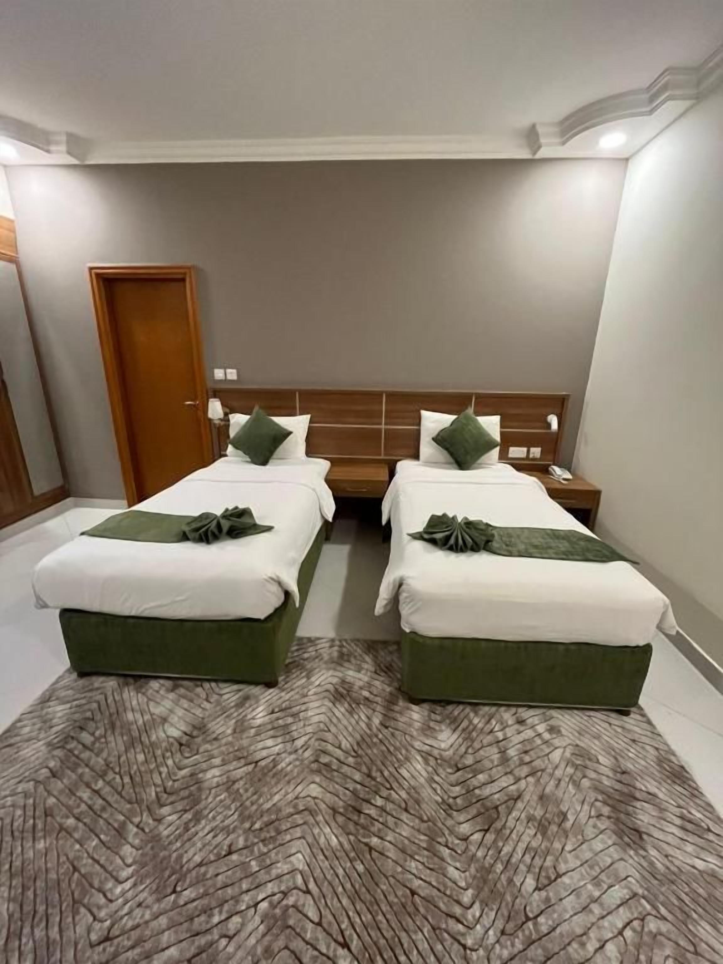 A hotel room with two beds, a wooden headboard, and a patterned rug.