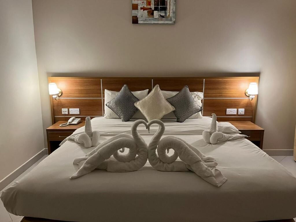 Quarto de hotel com cama bem arrumada, duas luminárias de cabeceira, telefone e uma obra de arte na parede.
