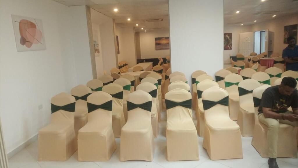 A conference room with rows of chairs and tables, a person seated, and a door in the background.