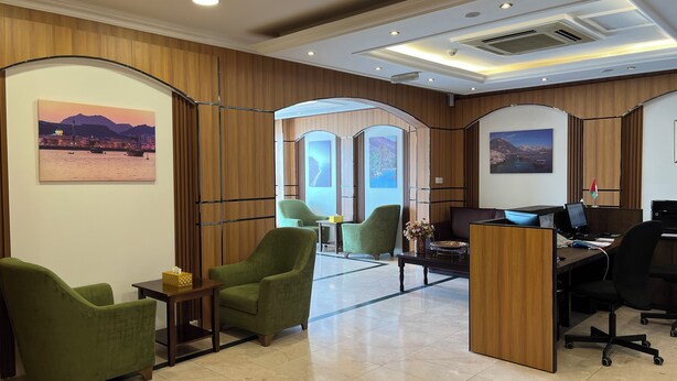 A modern office space with wooden paneling, green chairs, a desk with a computer, and framed artwork on the walls. - Al Murooj Hotel Apartments (Muscat)