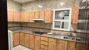 A kitchen with wooden cabinets, a gas stove, a sink, and a window with a fan. - Al Murooj Hotel Apartments (Muscat)