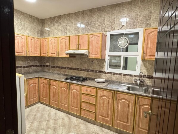 A kitchen with wooden cabinets, a gas stove, a sink, and a window with a fan.