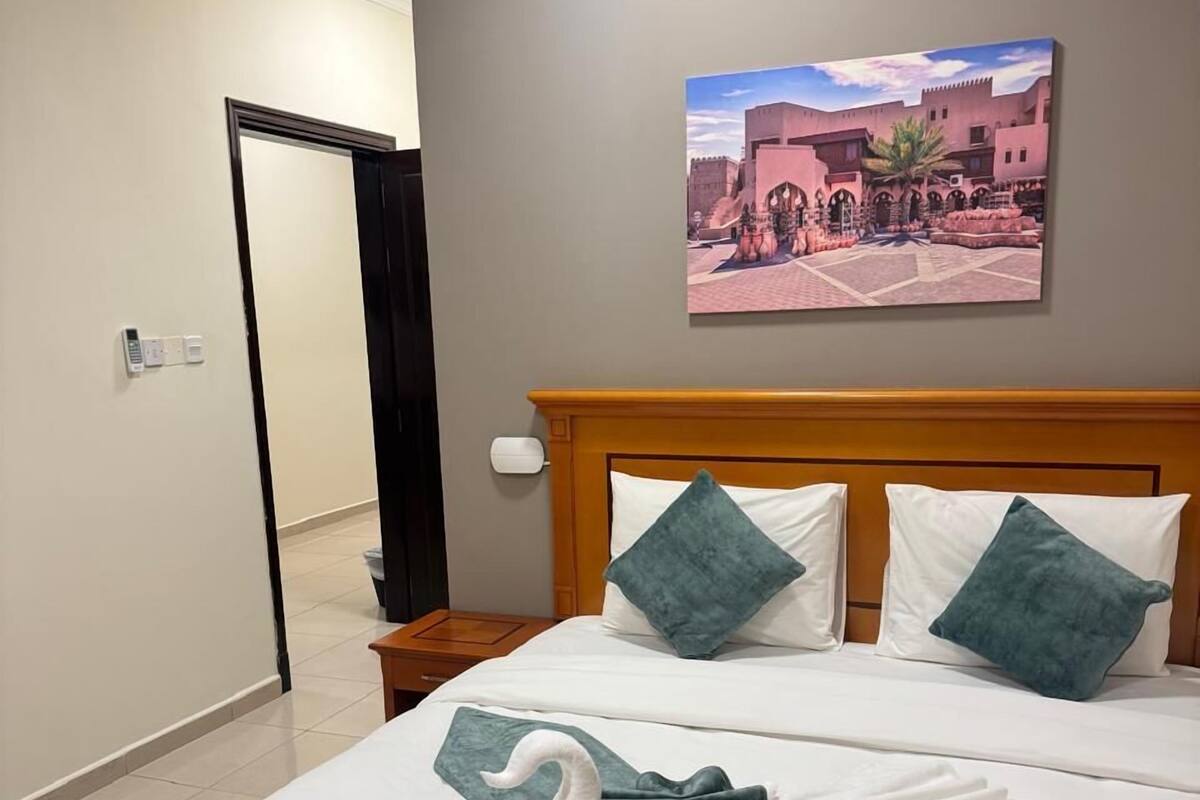 A hotel room with a bed, a painting of a building, and a door.