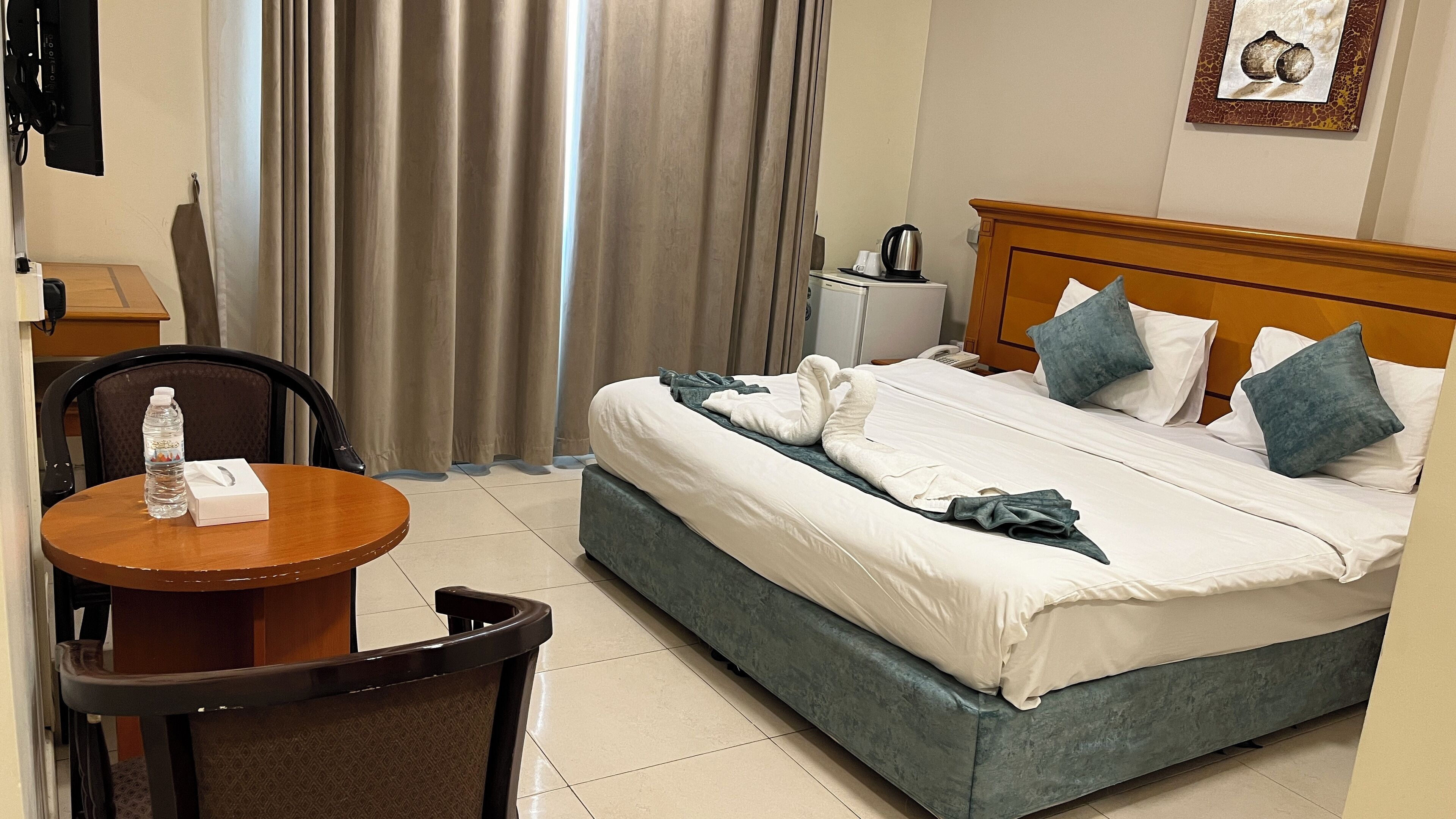 A hotel room with a bed, a table with a bottle and tissue box, a chair, and a coffee maker on the nightstand.