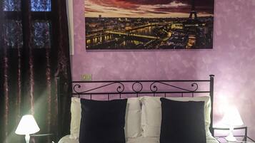 Una habitación de hotel con una cama, dos lámparas de noche, una mesita de noche, una ventana con cortinas y un cuadro de un paisaje urbano en la pared.
