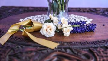 A table with a lace doily, a vase with white roses, purple flowers, and a gold ribbon.