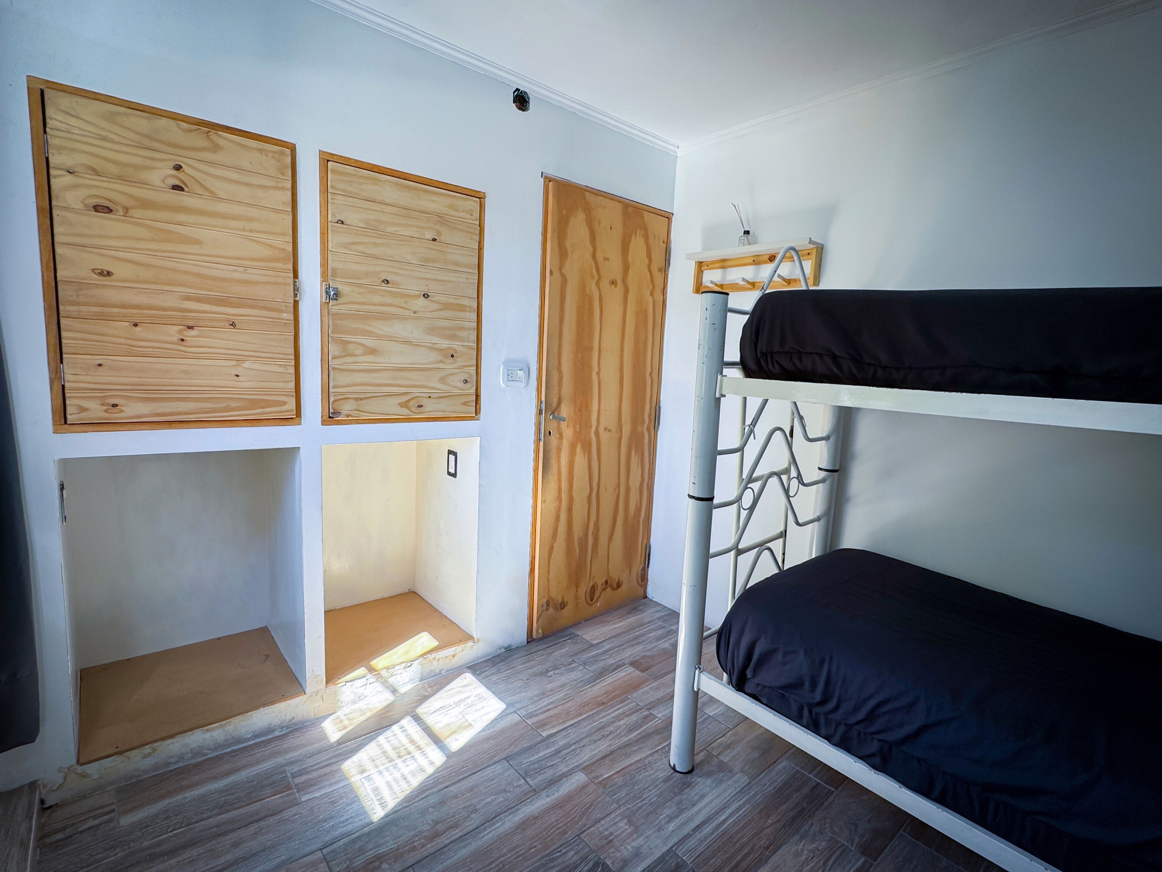 Habitación pequeña con literas, armario de madera y un rinconcito de escritorio.