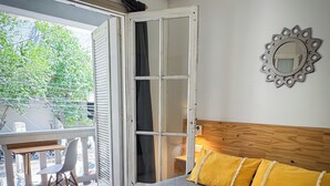 A hotel room with a bed, a wooden headboard, a window with a view of greenery, and an air conditioning unit on the wall. - Mora Hostel (Mendoza)
