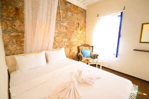 Une chambre d’hôtel avec un grand lit, un mur en pierre, une chaise et une fenêtre avec des rideaux.