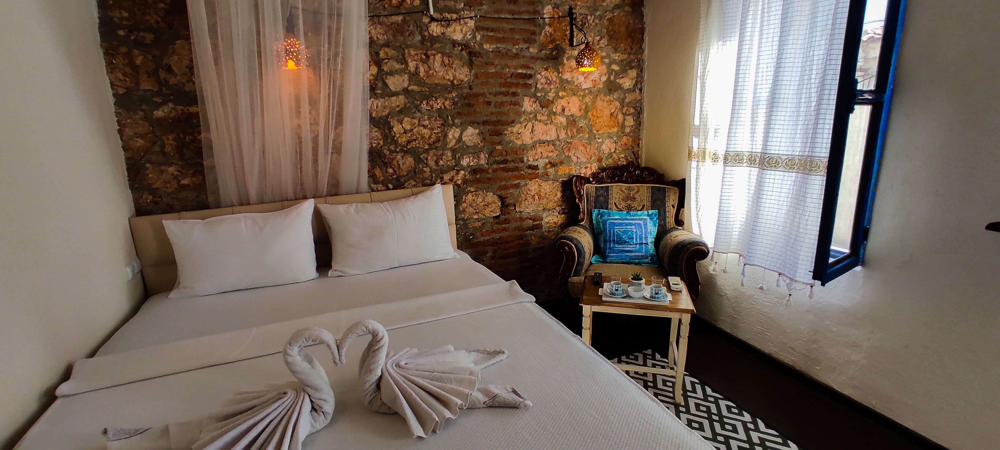 Una habitación de hotel con una cama grande, una mesita con lámpara, una silla y una ventana con cortinas.