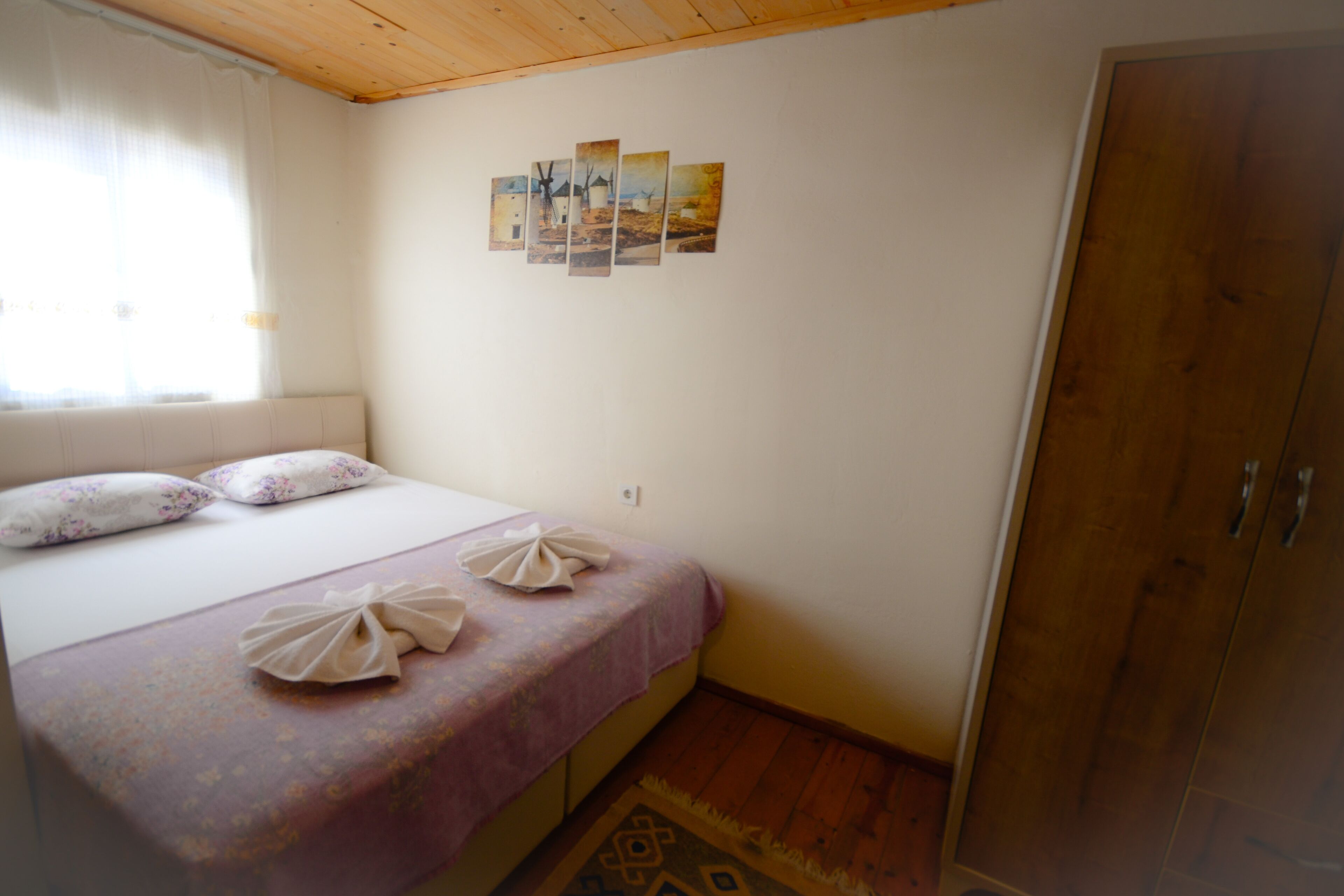 A bedroom with a bed, pillows, a wooden wardrobe, and a wall with a picture.