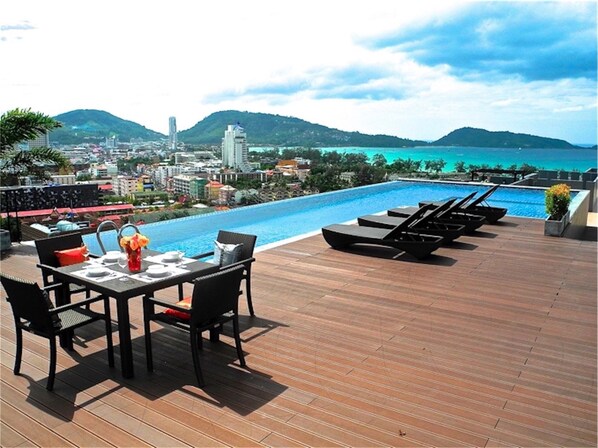 A rooftop pool area with a table and chairs, overlooking a cityscape and the sea.